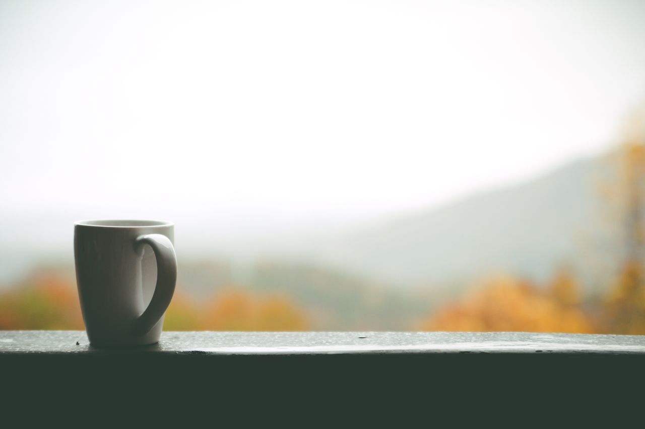 A solitary coffee mug on a balcony overlooks a foggy autumn landscape.