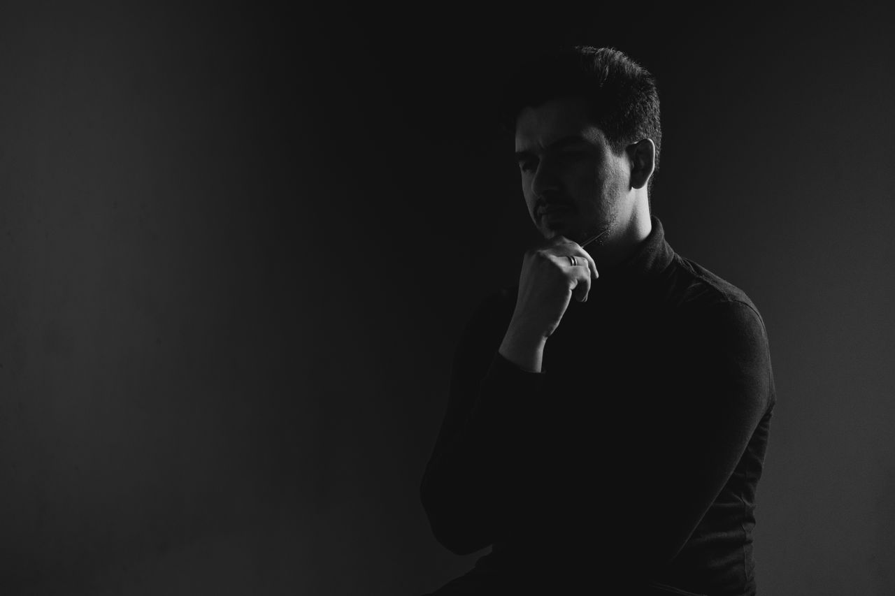 Stylish black and white studio portrait of a man in thoughtful pose.